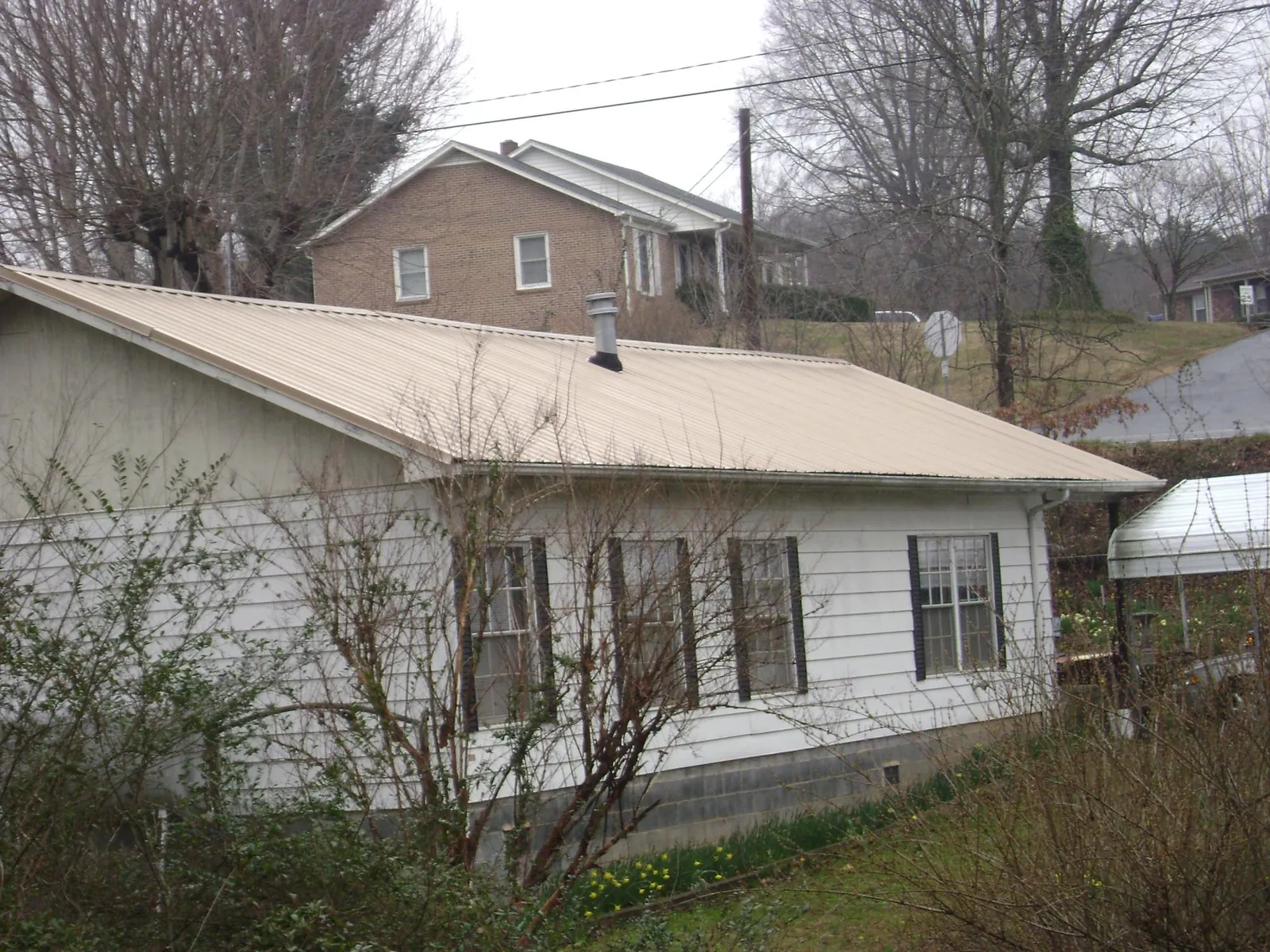 Tan metal roof on a white sided house set into a hillside — Commercial Roofing by Roofing Brothers in Oceanside